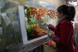 An artist in the Nan'an factory working on popular palette knife paintings popularized by Leonid Afremov